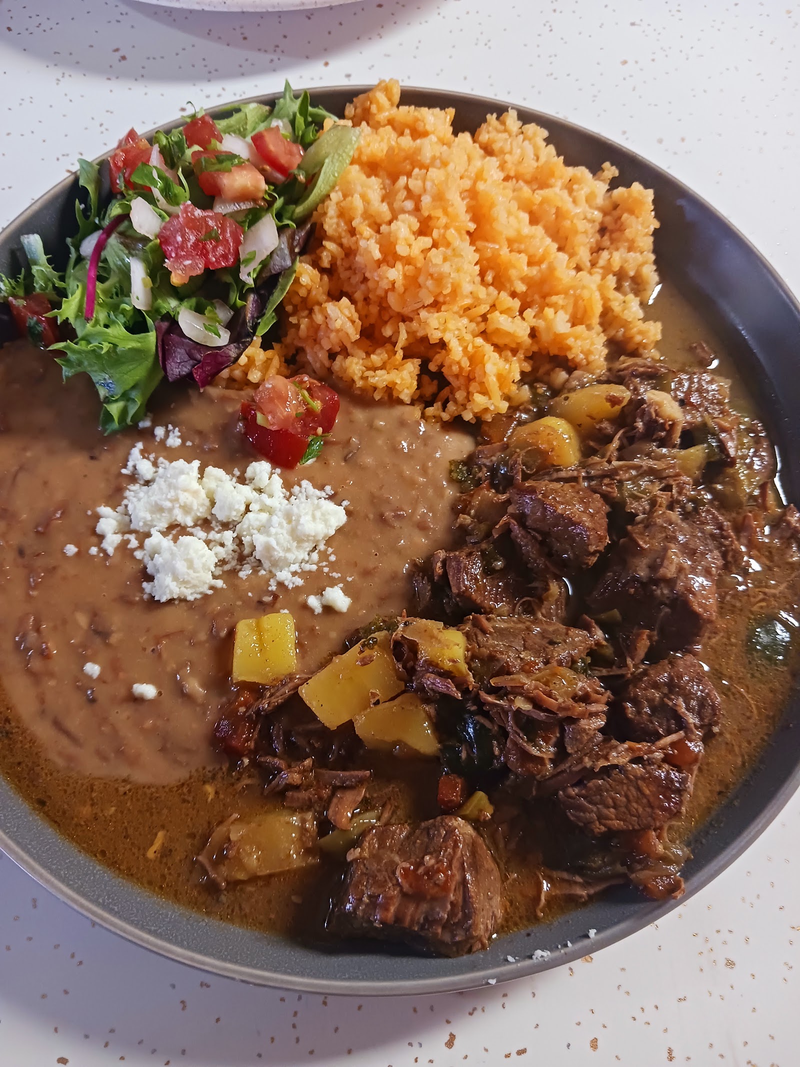 Carne guisada bowl with Mexican rice, refried beans, and a fresh garden salad